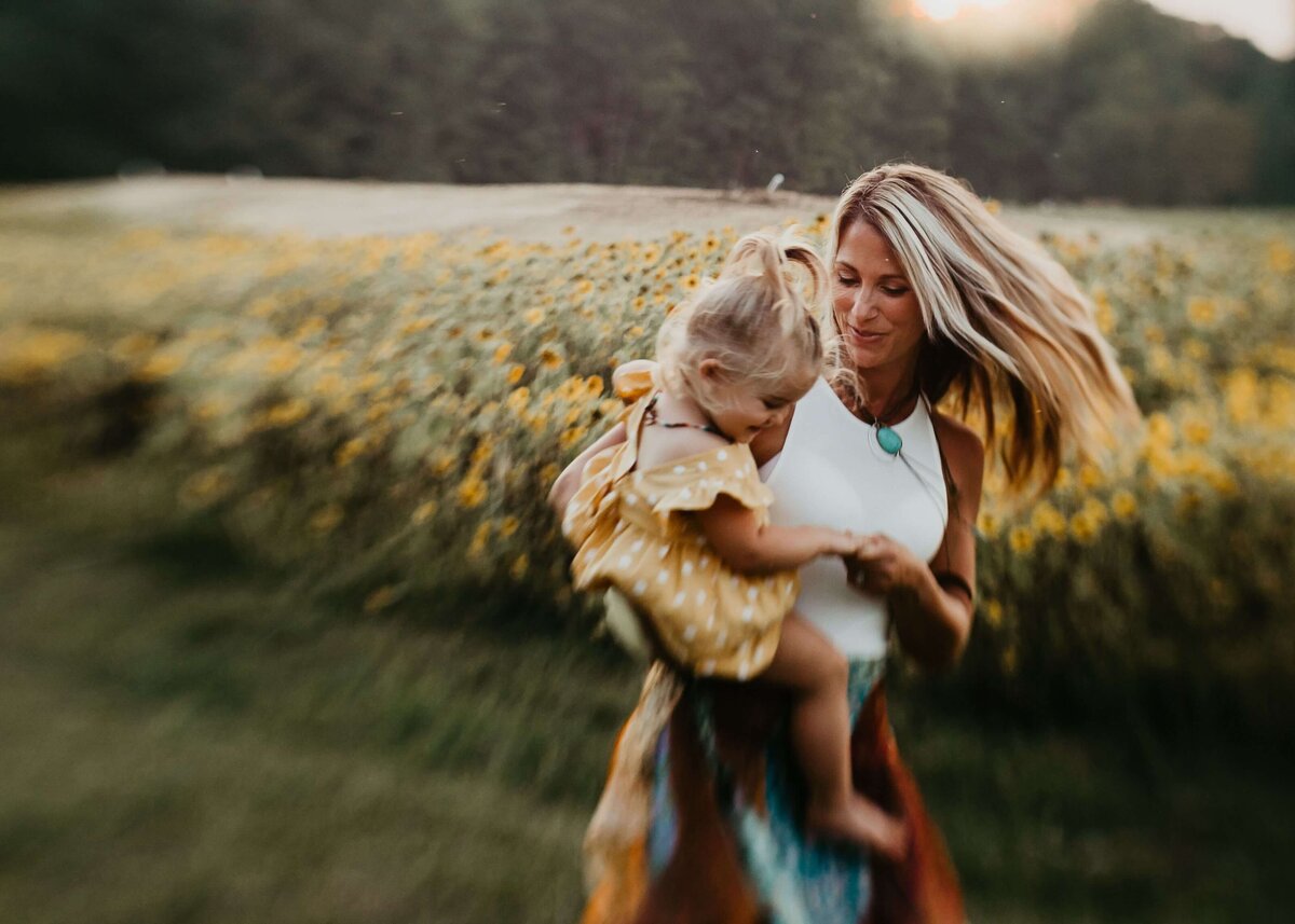 A mother and daughter joyfully running through a field of sunflowers, captured by a Pittsburgh family photographer.