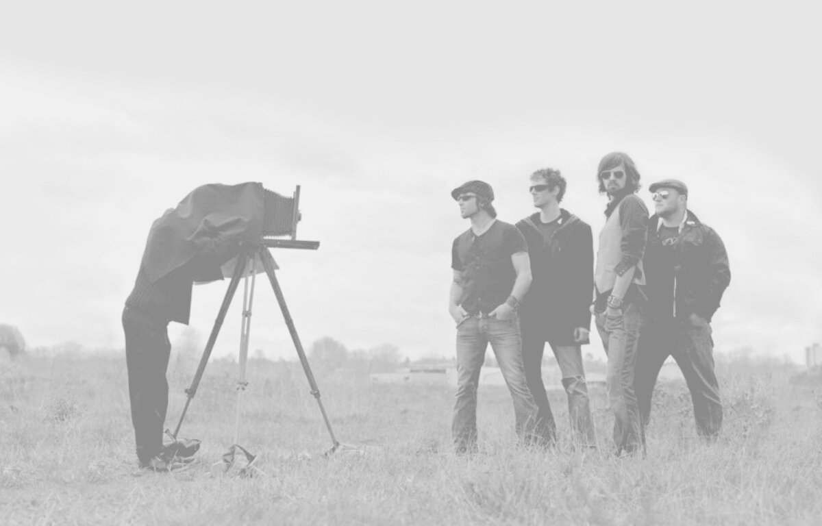 Photography Business Basics Book Cover Image Photographer standing behind bellowed camera on tripod with cloth over his head photographing four men standing in grass field in black and white