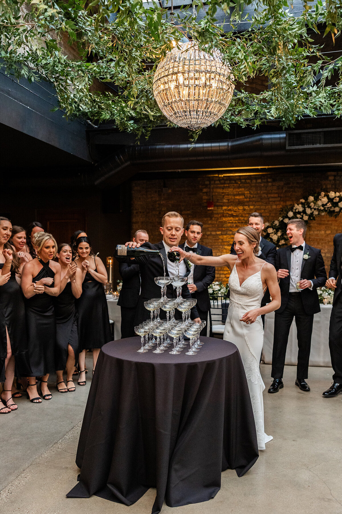 ride and groom pour champagne into a tower of glasses at their wedding reception