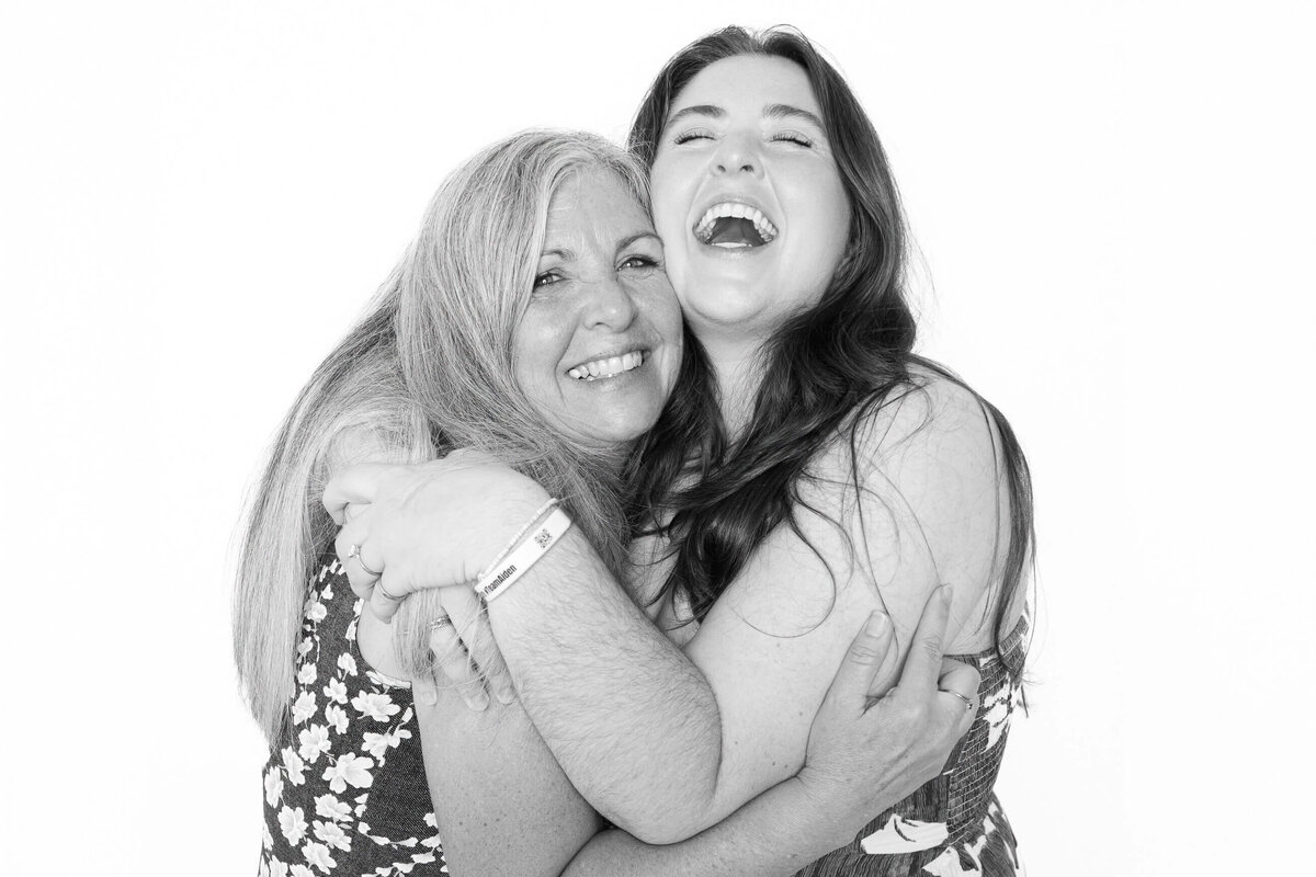 Mother and daughter embracing and laughing in a black and white photo booth portrait captured by Monochrome Portraits, a modern Phoenix photo booth experience.