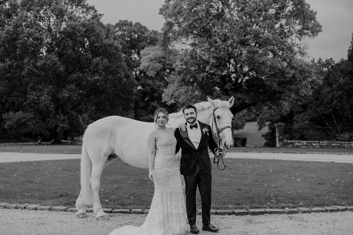 Black and white image of Bride and groom in front of a white horse for their Ireland wedding
