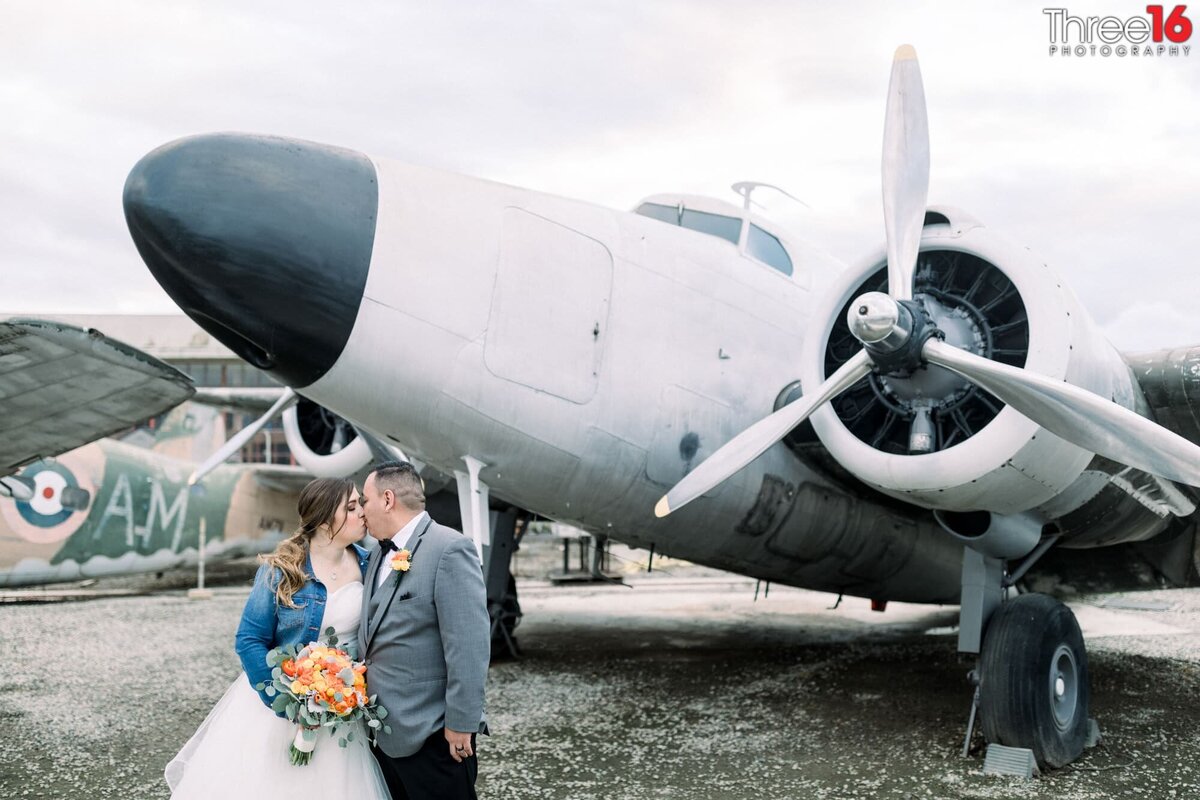 Bride and Groom share a big kiss standing in front of a vintage war plane