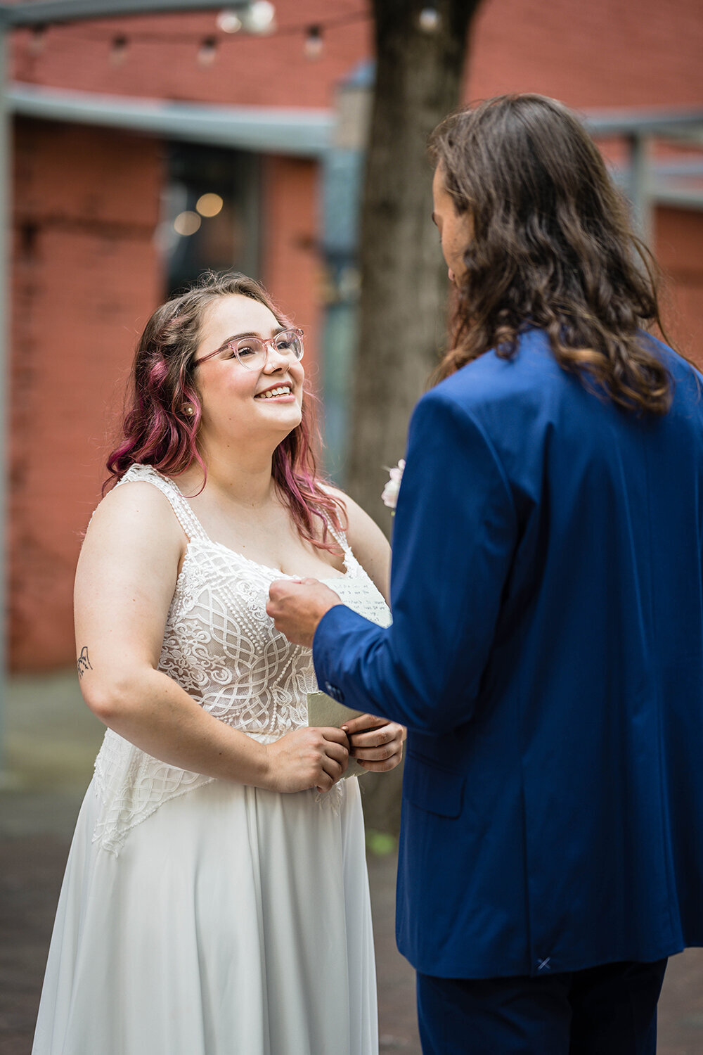 A bride smiles widely at the groom as he reads his vows to her during the ceremony on their elopement day in a tea-light lit alleyway in Downtown Roanoke.