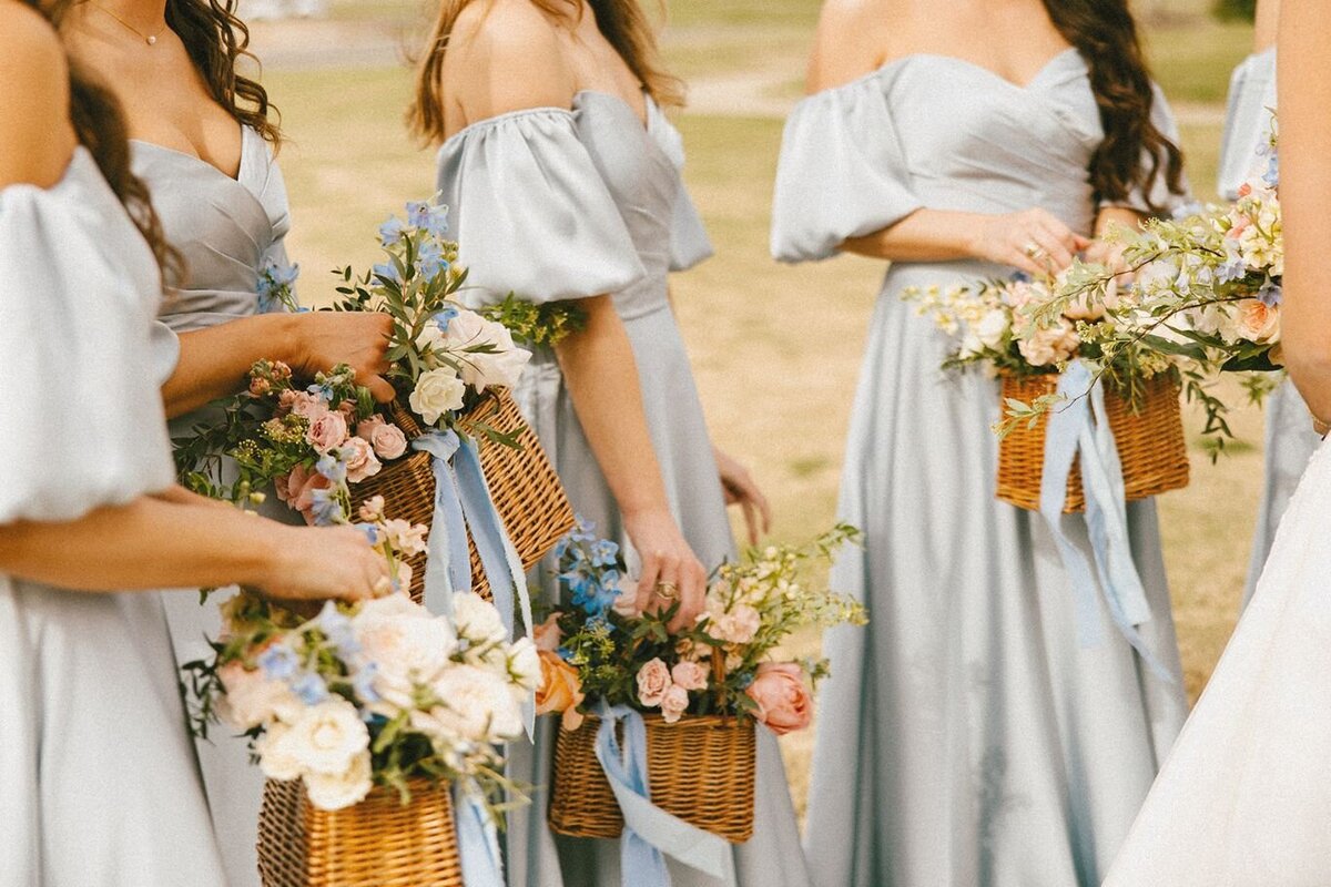 Bridesmaids wearing light blue dresses holding basket bouquets with pastel florals and blue ribbon details