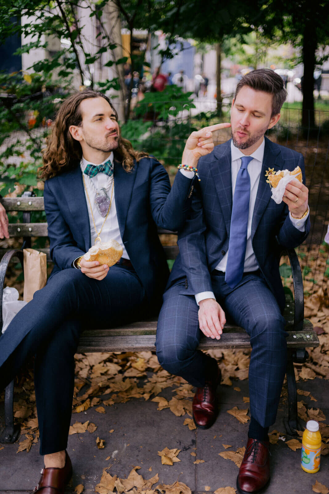 The two grooms are eating burger while sitting on a park bench after the ceremony. NYC City Hall Elopement Image by Jenny Fu Studio