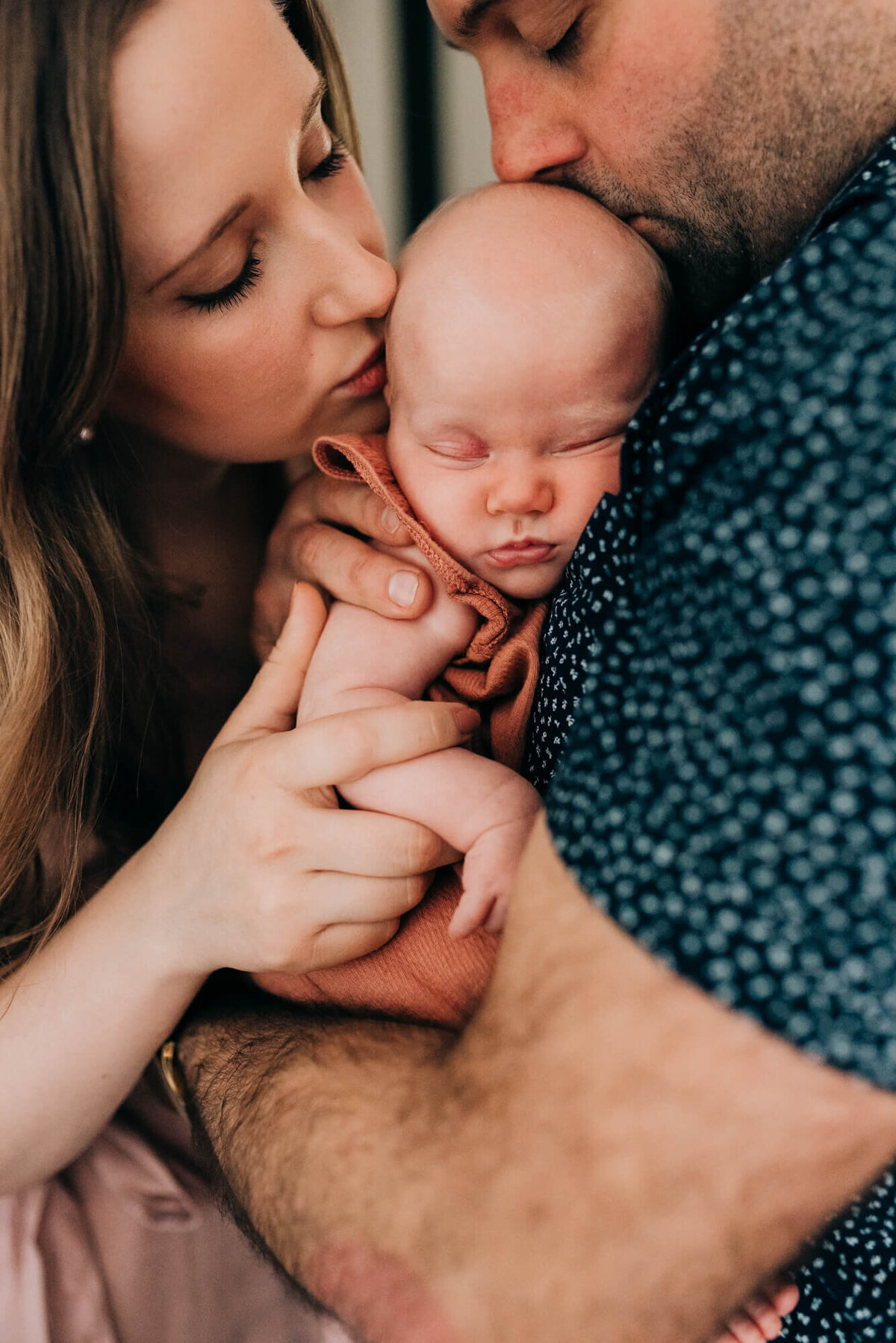 A close up of a young couple kissing their newborn baby together during their photoshoot with Boston Newborn Photographer, Allison Wolf