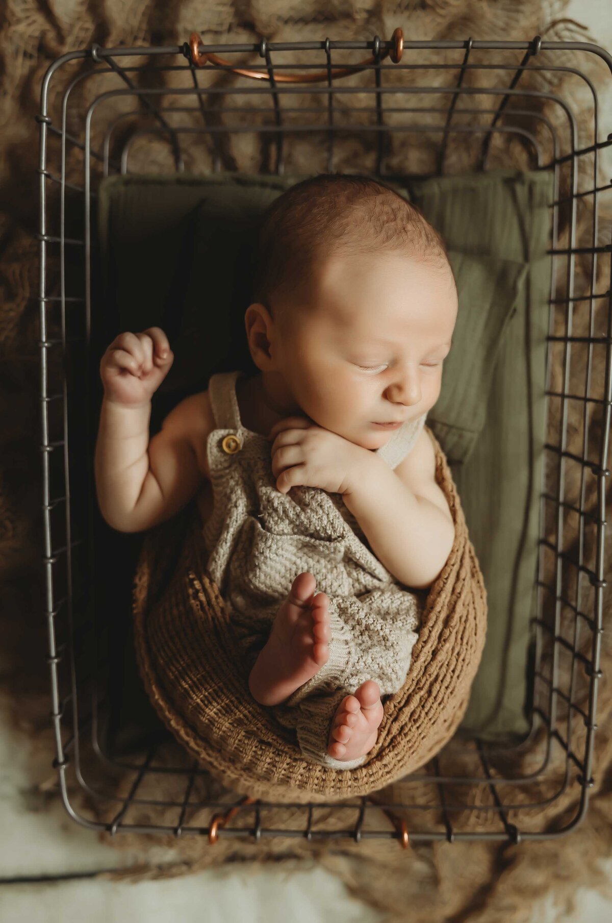 Nweborn baby wearing a gray overall sleeping inside a basket