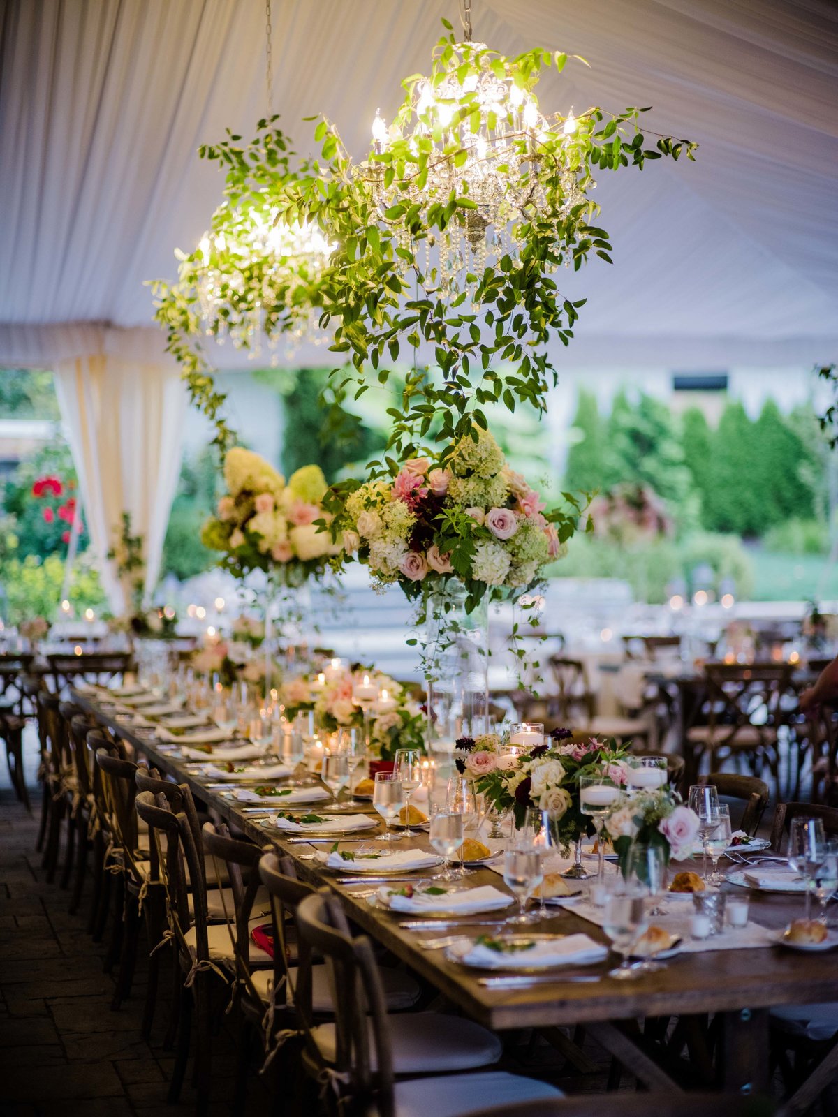 Green smilax covered chandeliers hang from the tent in this romantic garden wedding designed by Flora Nova.
