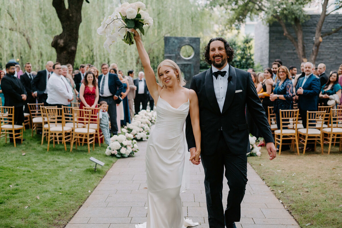 Bride and groom walk joyfully down the aisle after outdoor wedding ceremony, surrounded by cheering guests