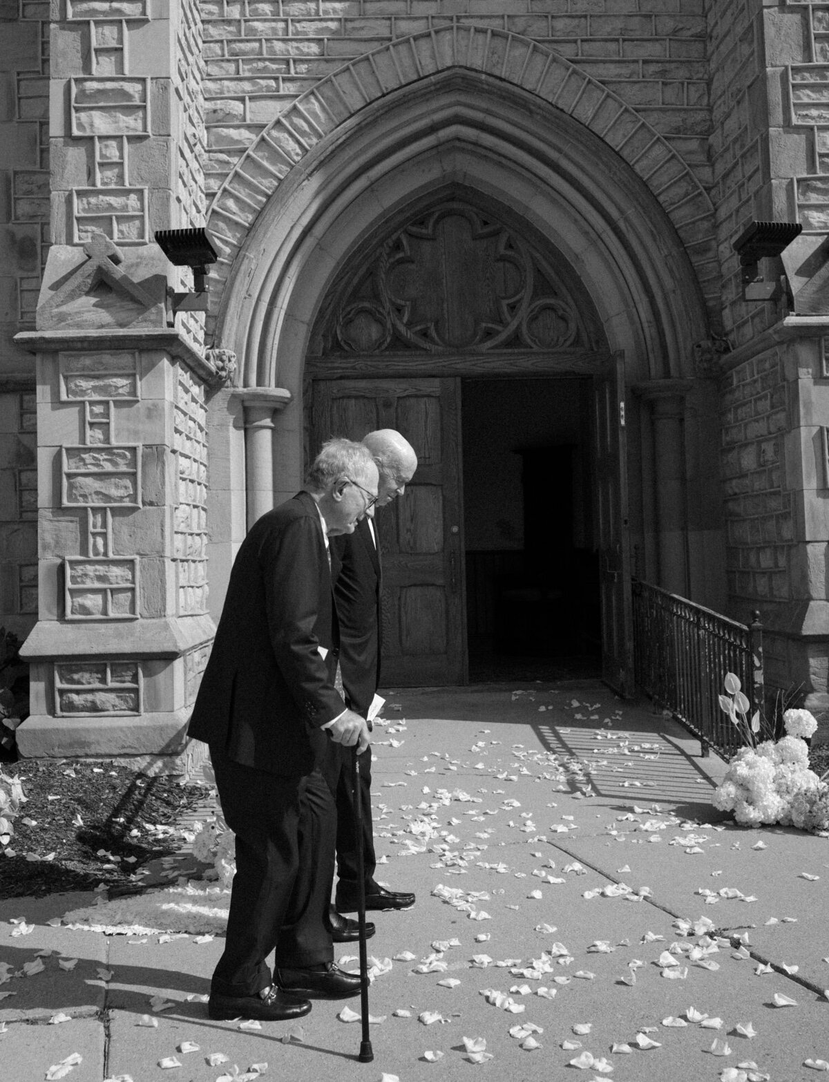 documentary style wedding photography shows two old men with canes walking across scattered petals at Christ Church, Detroit