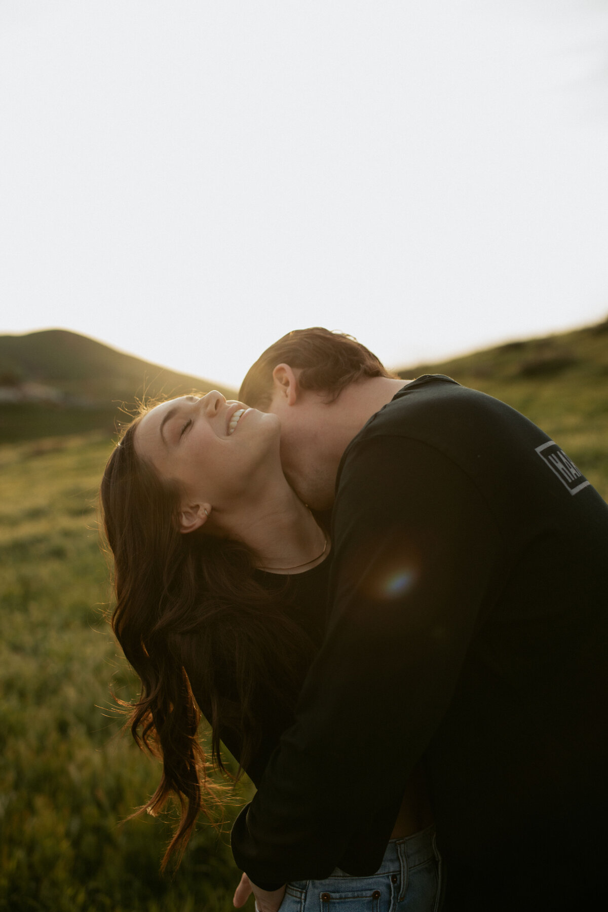 couples photos in big green field kissing her neck