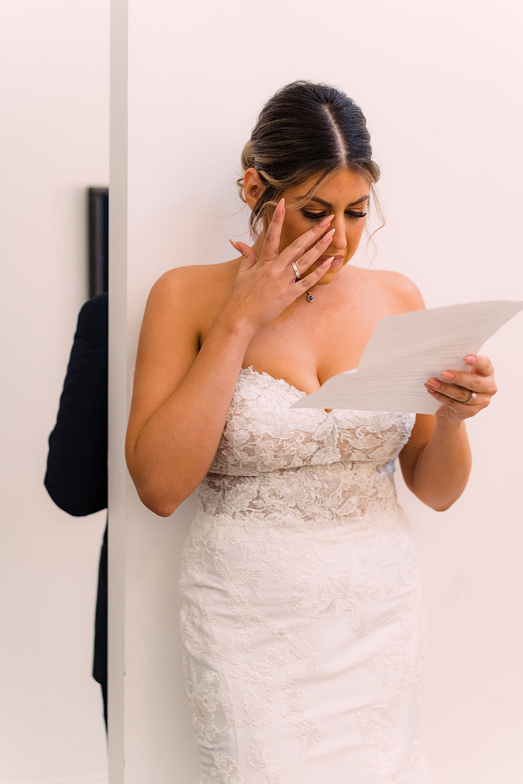 Bride, touched with emotion, holds a letter close while wiping away tears in a quiet, tender moment.