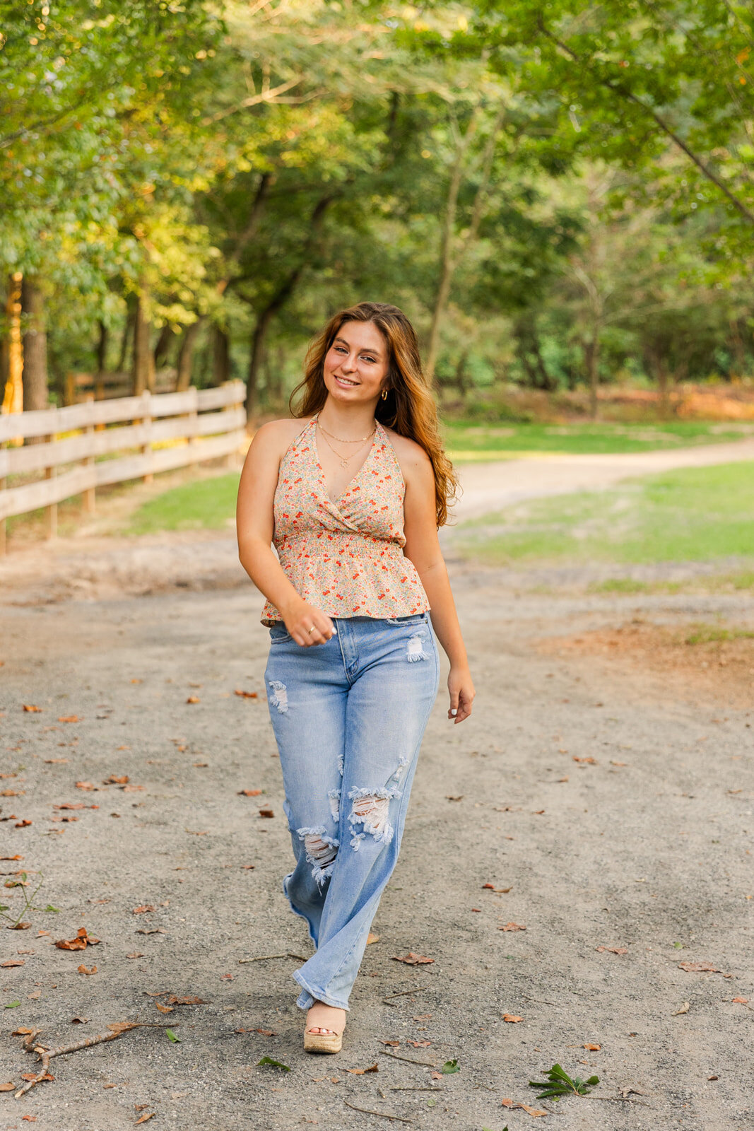 senior girl wearing jeans and printed top walking toward the camera on a park path during photo portraits