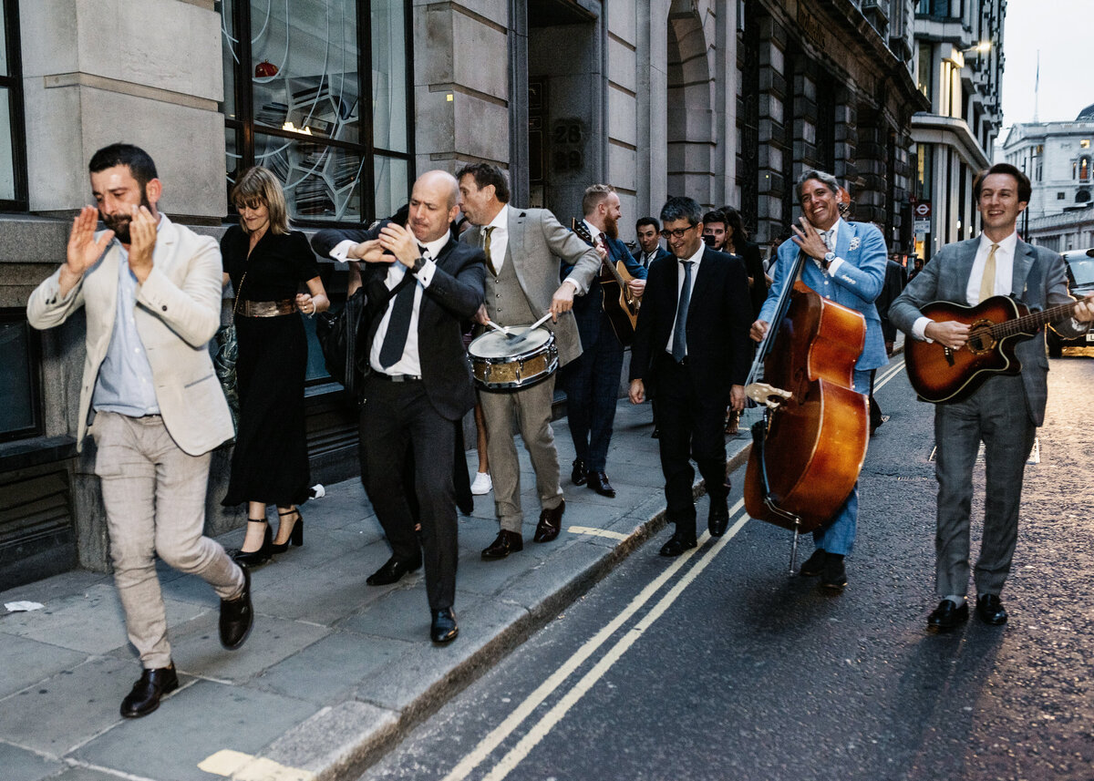A roaming band play their instruments alongside wedding guests in the street at a party in London.
