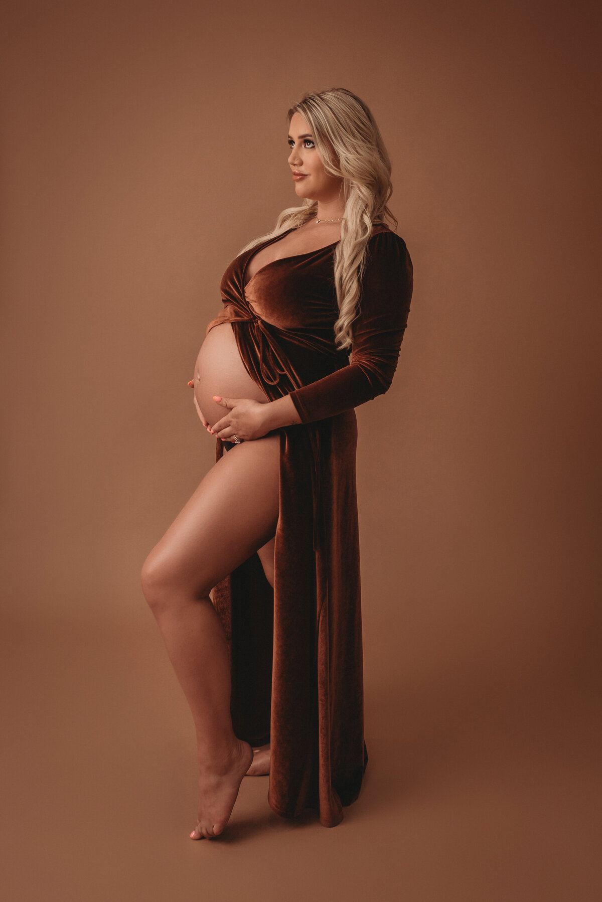 Atlanta, Georgia newborn photographer portrait session with pregnant woman at maternity session holding pregnancy tummy pose wearing copper velvet dress