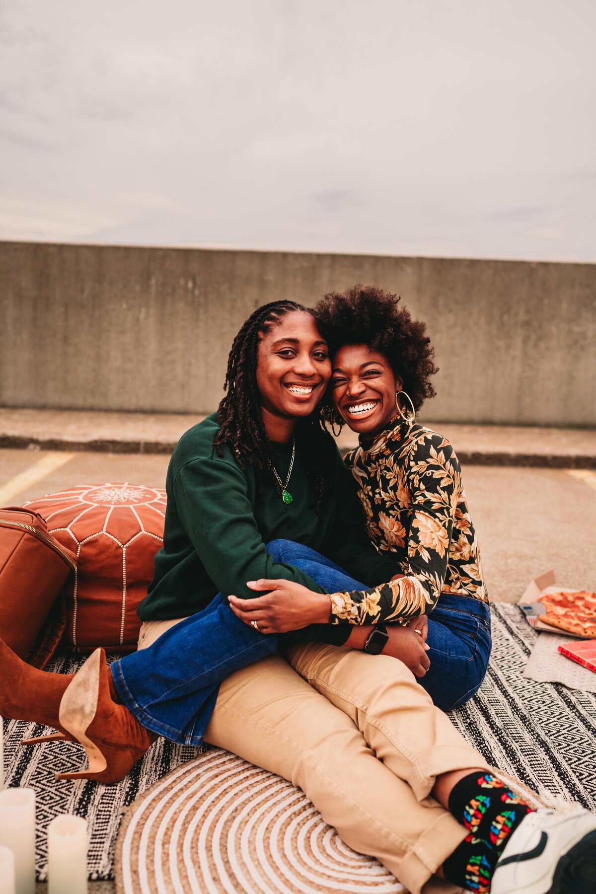 A queer couple cuddles on a rooftop picnic, sharing laughter & love in a candid, moody editorial-style session in Erie.