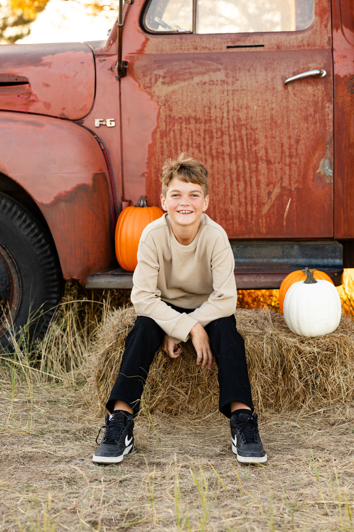 A pre-teen boy sits on the step of a vintage red farm truck and smiles at the camera.