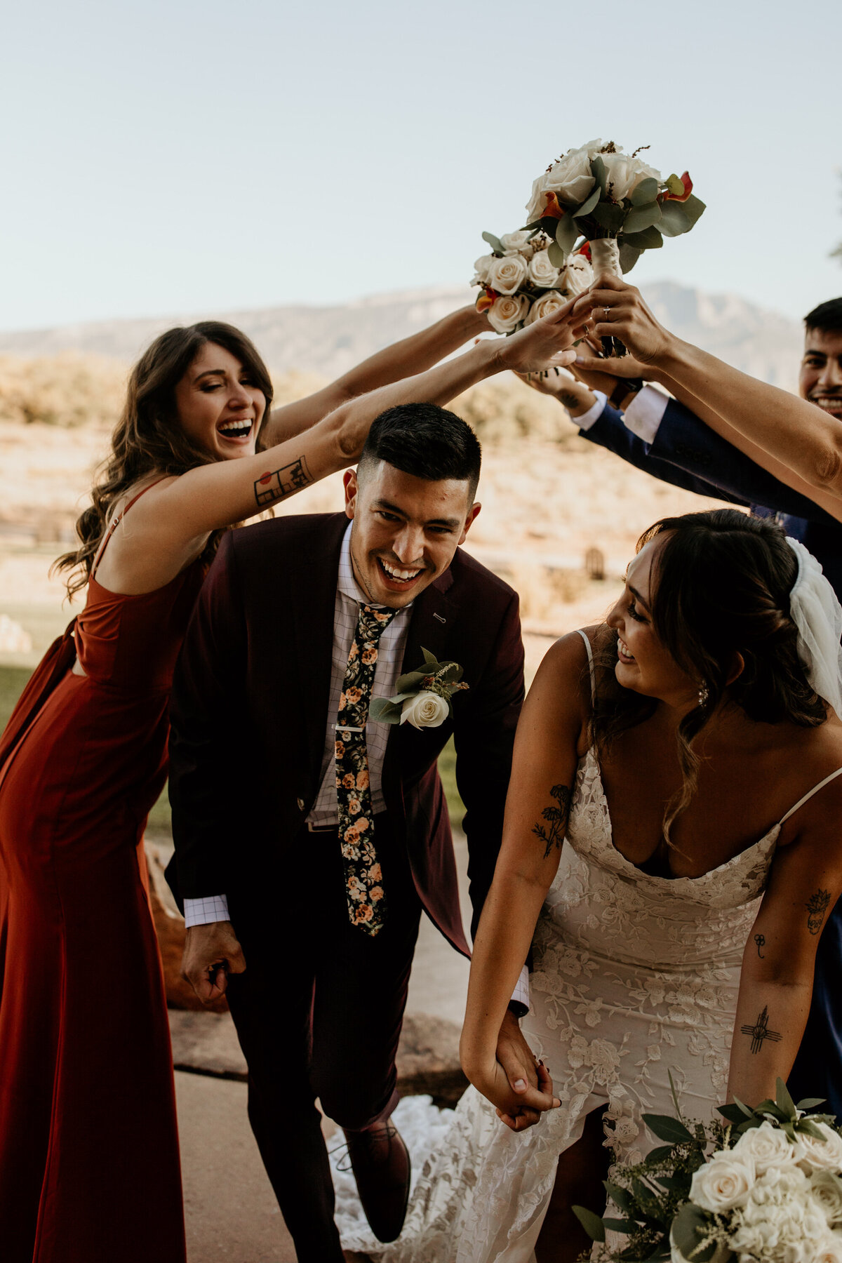 bride and groom walking under their wedding parties arms in the desert