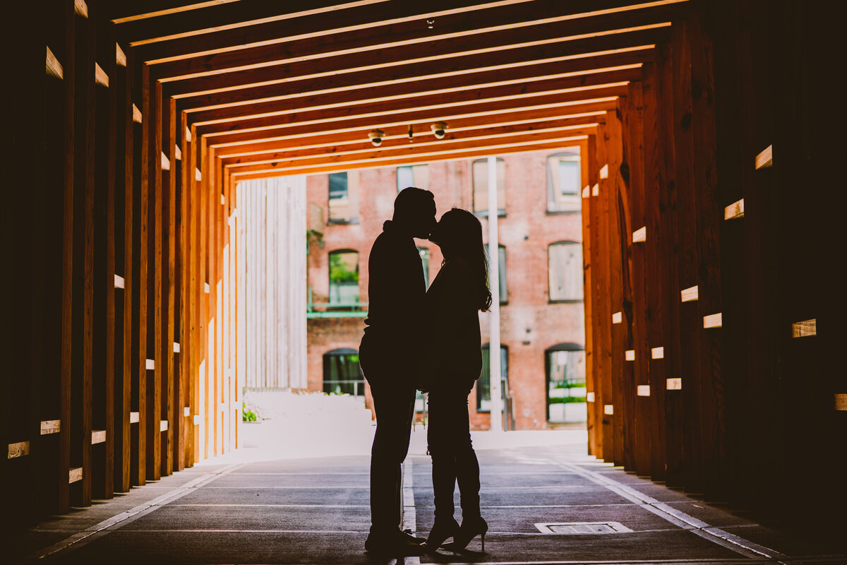 A couple kissing under a wood tunnel near the 1 hotel at brooklyn bridge park in dumbo