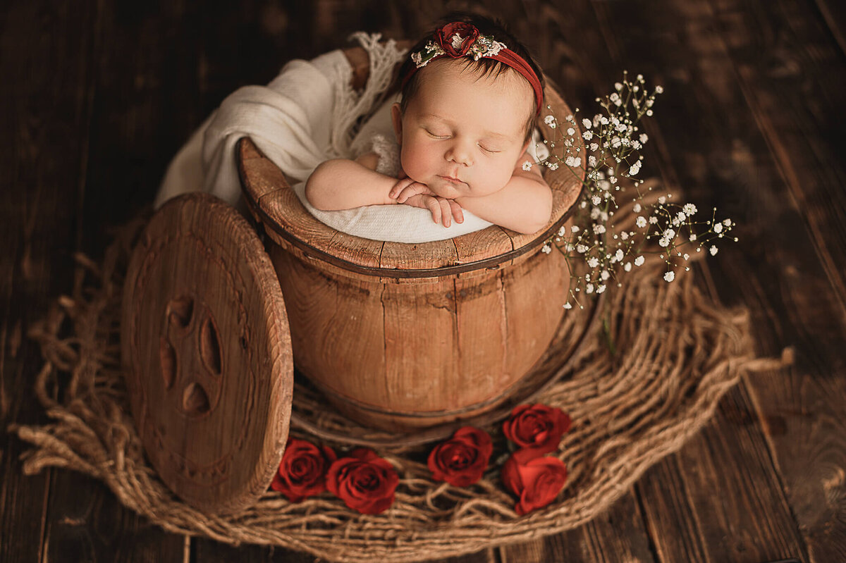 Baby girl sleeping in a wood bucket with red roses.
