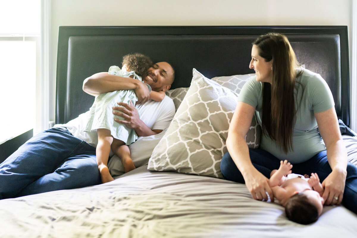 Family with toddler and newborn boy playing on bed