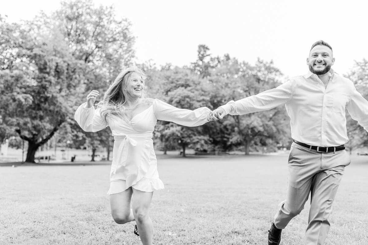 black and white photo of engaged couple running in a field at Congress Park in Saratoga Springs, NY