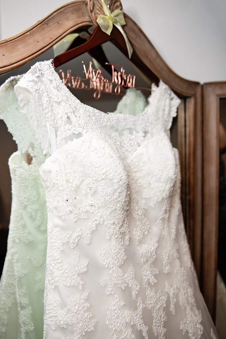 Wedding dress with lace accents hanging on a Mrs hanger on antique mirror
