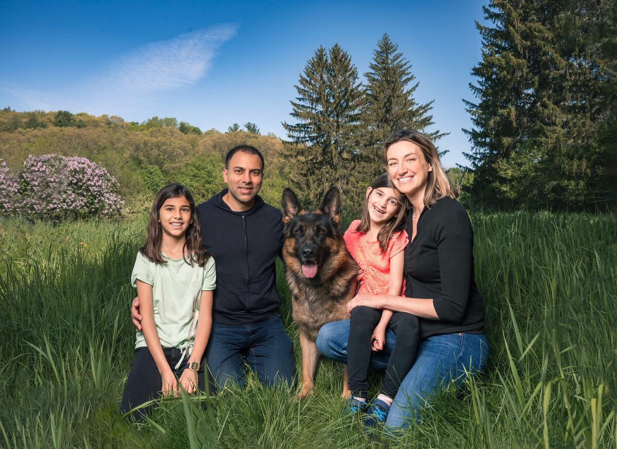Mixed race family portrait with dog in Lincoln, MA field with blue sky and trees