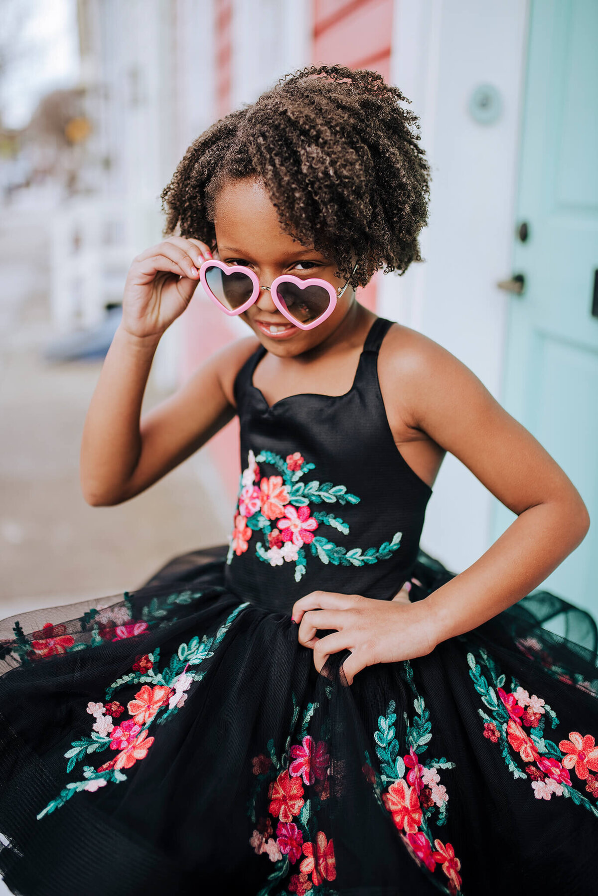 African American Girl wearing a black floral dress looking over the top of pink hearts glasses in Fells Point Baltimore Maryland
