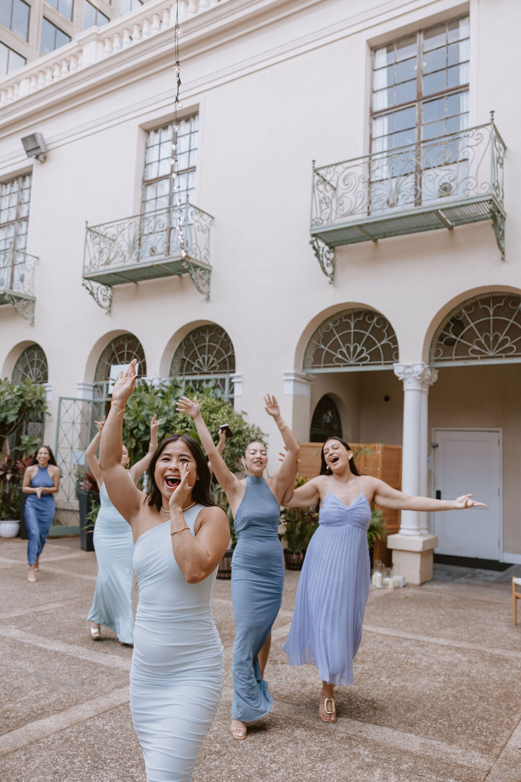 Bridesmaids cheering while walking all wearing blue dresses in front of european style building