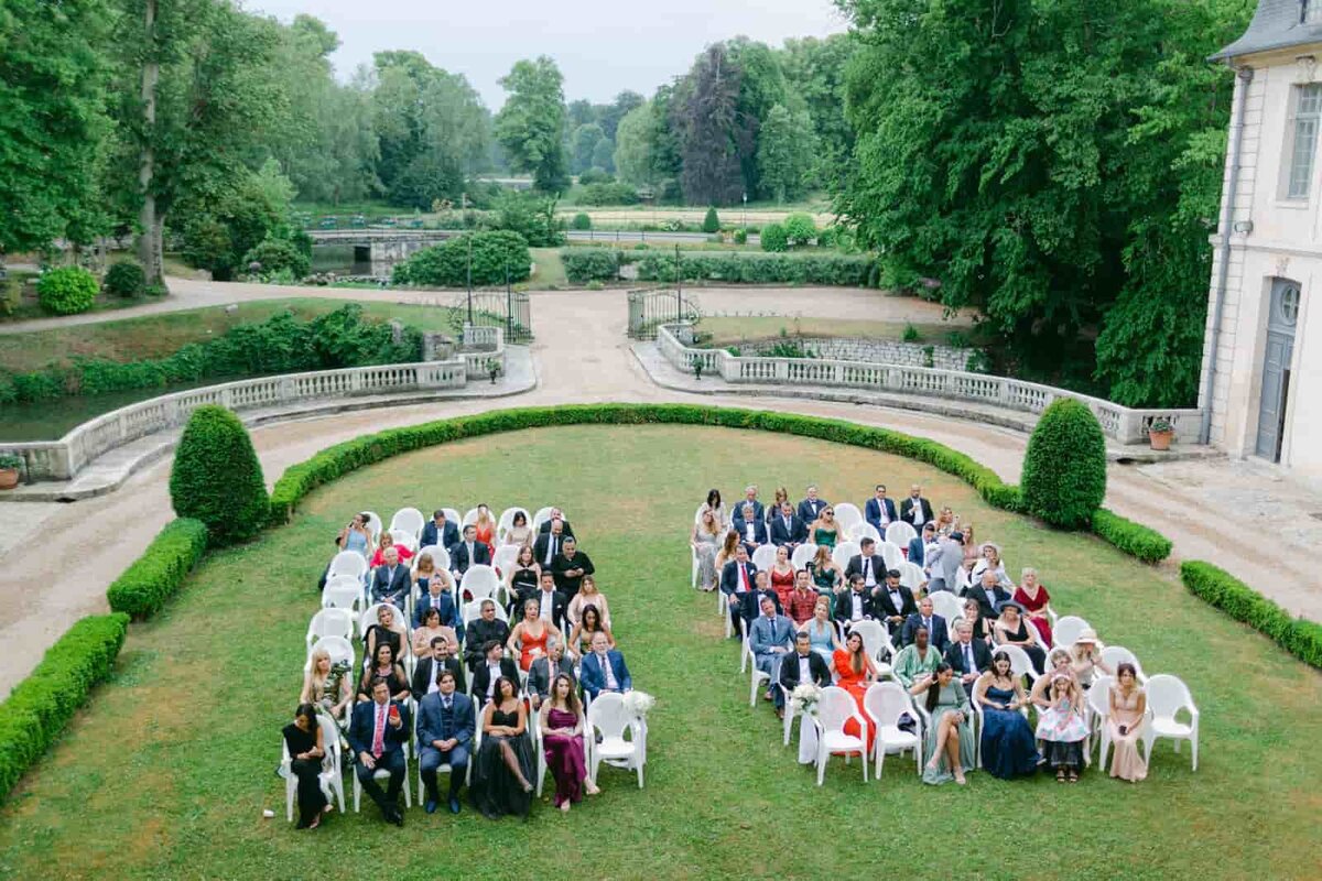 Wedding guests seated outdoors in a symmetrical garden setting, beautifully documented by Paris wedding photographer Thomas Raboteur