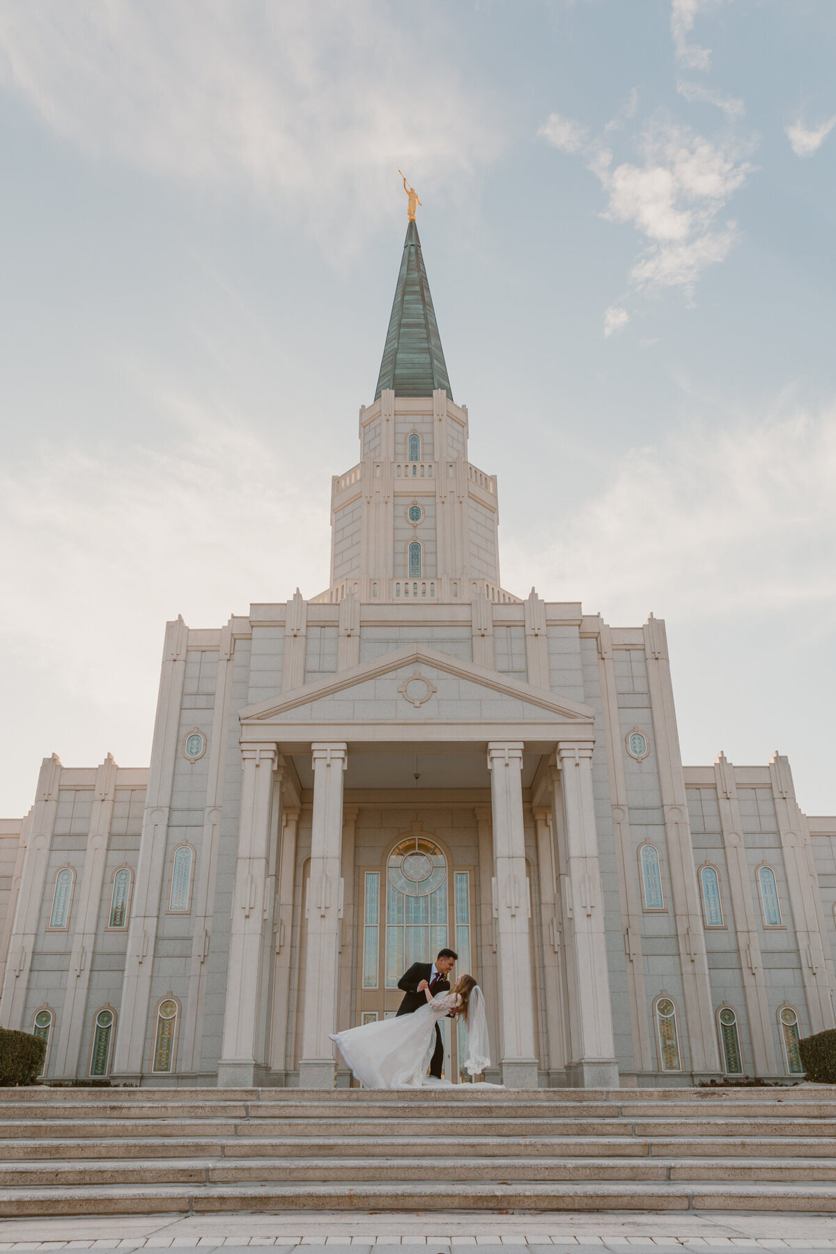 Newlywed couple sharing a romantic dip pose outside the Houston LDS Temple. Elegant architecture and grand entrance in the background. 