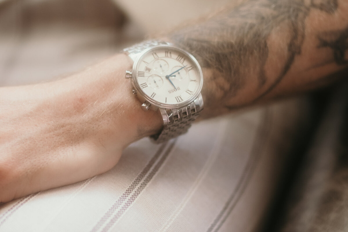 Diese Nahaufnahme zeigt die silberne Uhr der Marke Boss am Handgelenk des Bräutigams.
