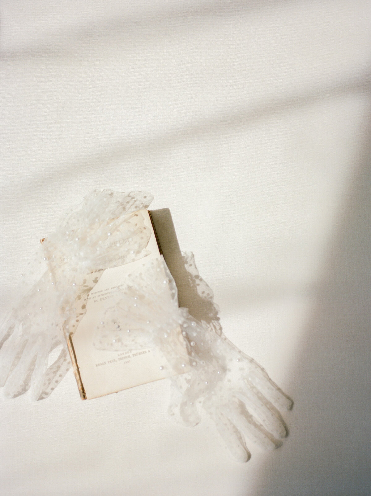 ethereal film flat lay, tulle gloves with pearls, antique book, directional light