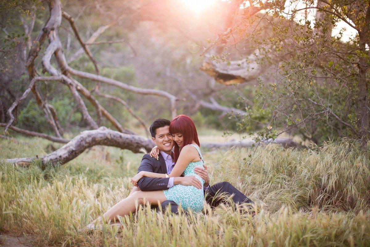 Bride to be sits on her Groom's lap as they cuddle for engagement photos at Irvine Regional Park