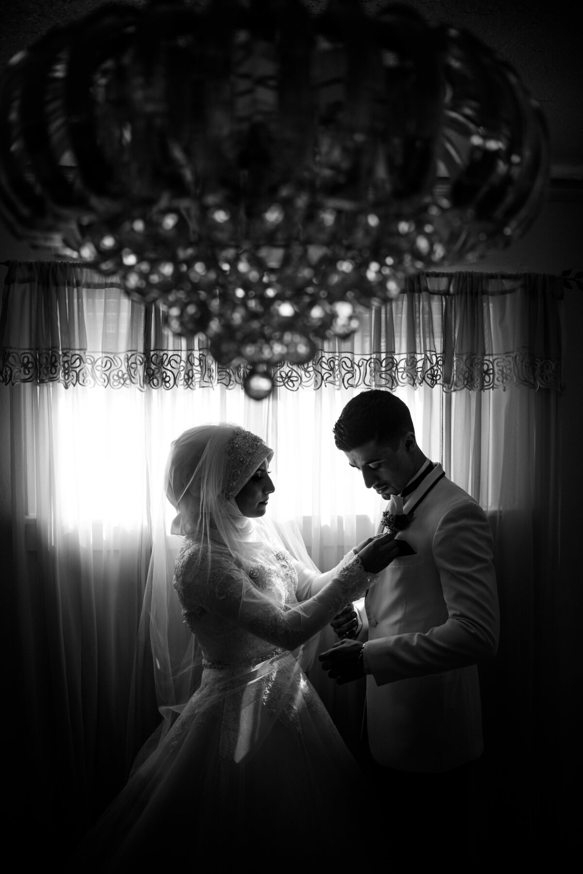 Couple enjoying a quiet moment on their wedding day backlit by a window with a crystal chandelier.