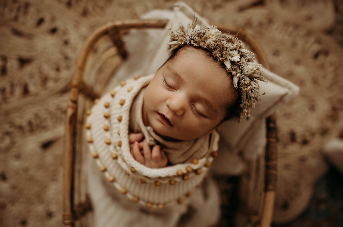 Newborn baby wrapped in a rust colored crochet blanket and matching hat sleeping in a basket.