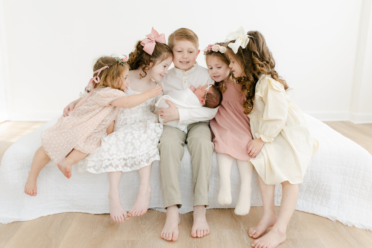 five siblings gathered around holding their new baby sister during their newborn session photographed by Philadelphia Newborn Photographer tara Federico