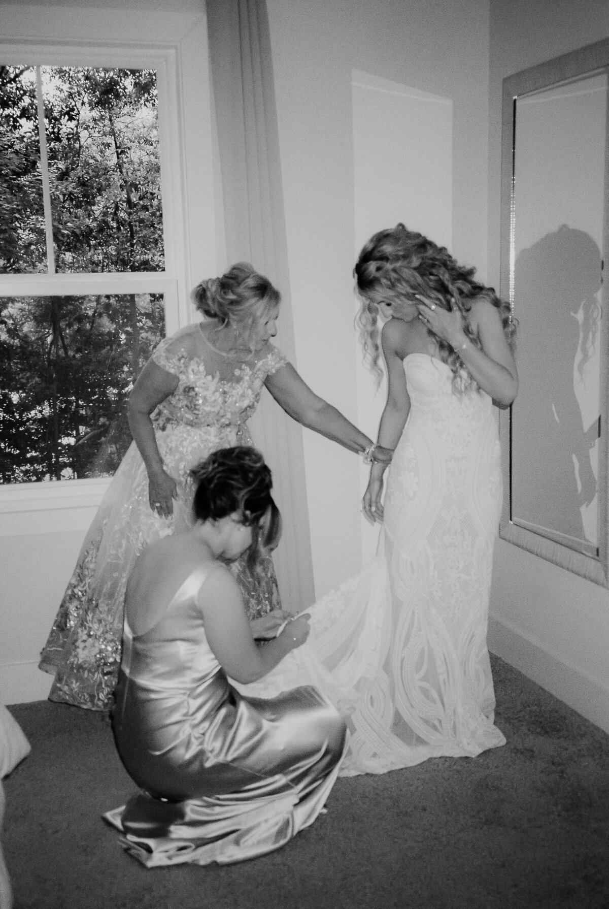 Bride getting into dress with mother of bride and bridesmaid assisting. Captured by Charleston Film Photographers