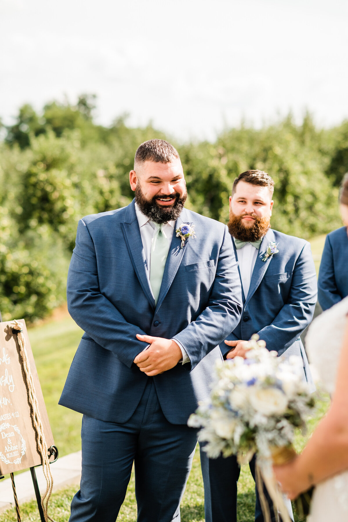 Groom watching his bride walk down the aisle on their outdoor wedding ceremony day and smiling as she approaches him captured by Virginia wedding photographer