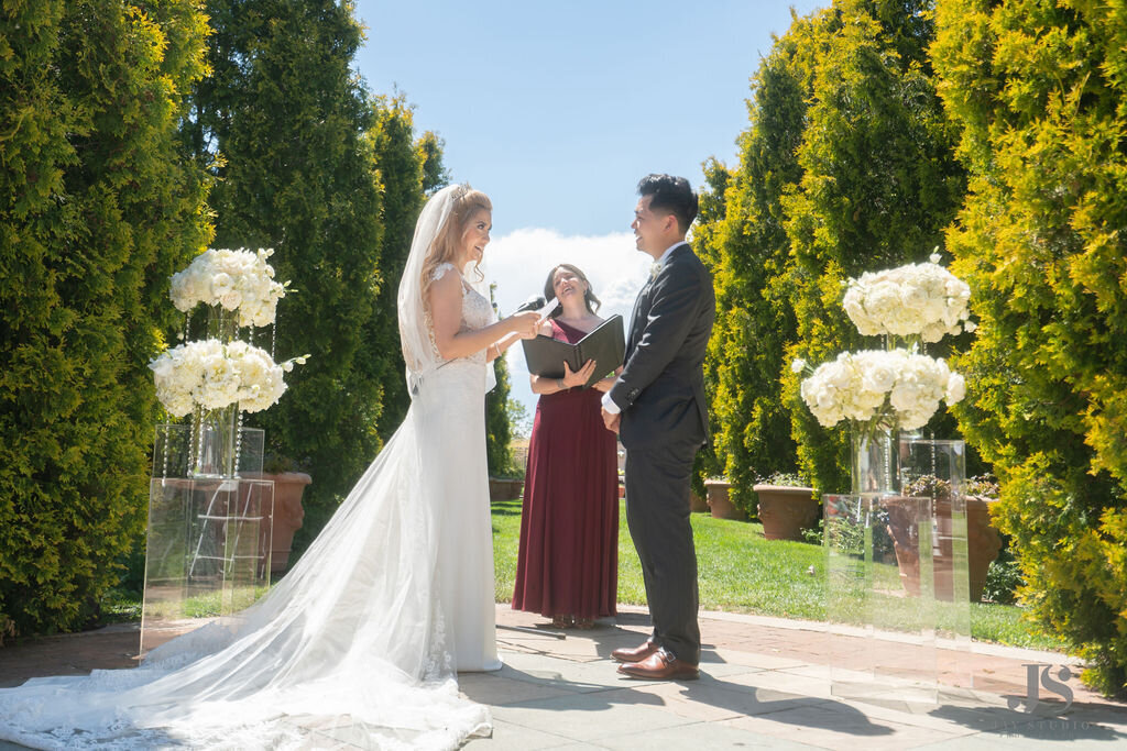 A bride and groom share vows during their ceremony with white flower arrangements on clear acrylic podiums at the Denver Botanic Gardens.