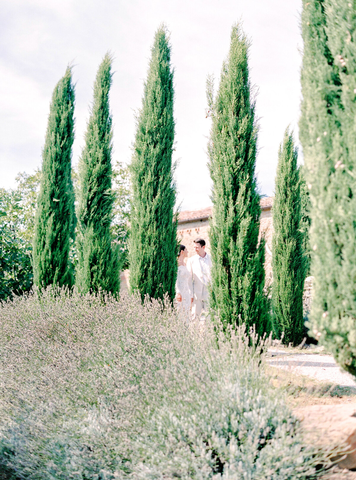 Film photograph of Bride and groom walking down a path of cypress trees photographed by Italy wedding photographer at Villa Montanare Tuscany wedding