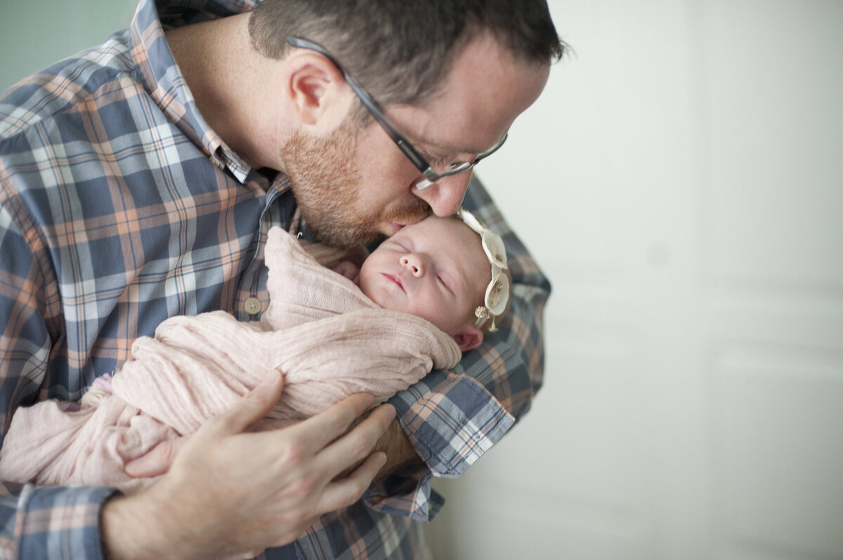 A parent holding their newborn and kissing them 