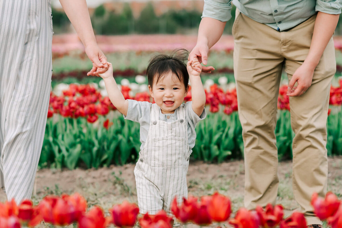 A little boy in white overalls smiling among the tulips at Burnside Farms