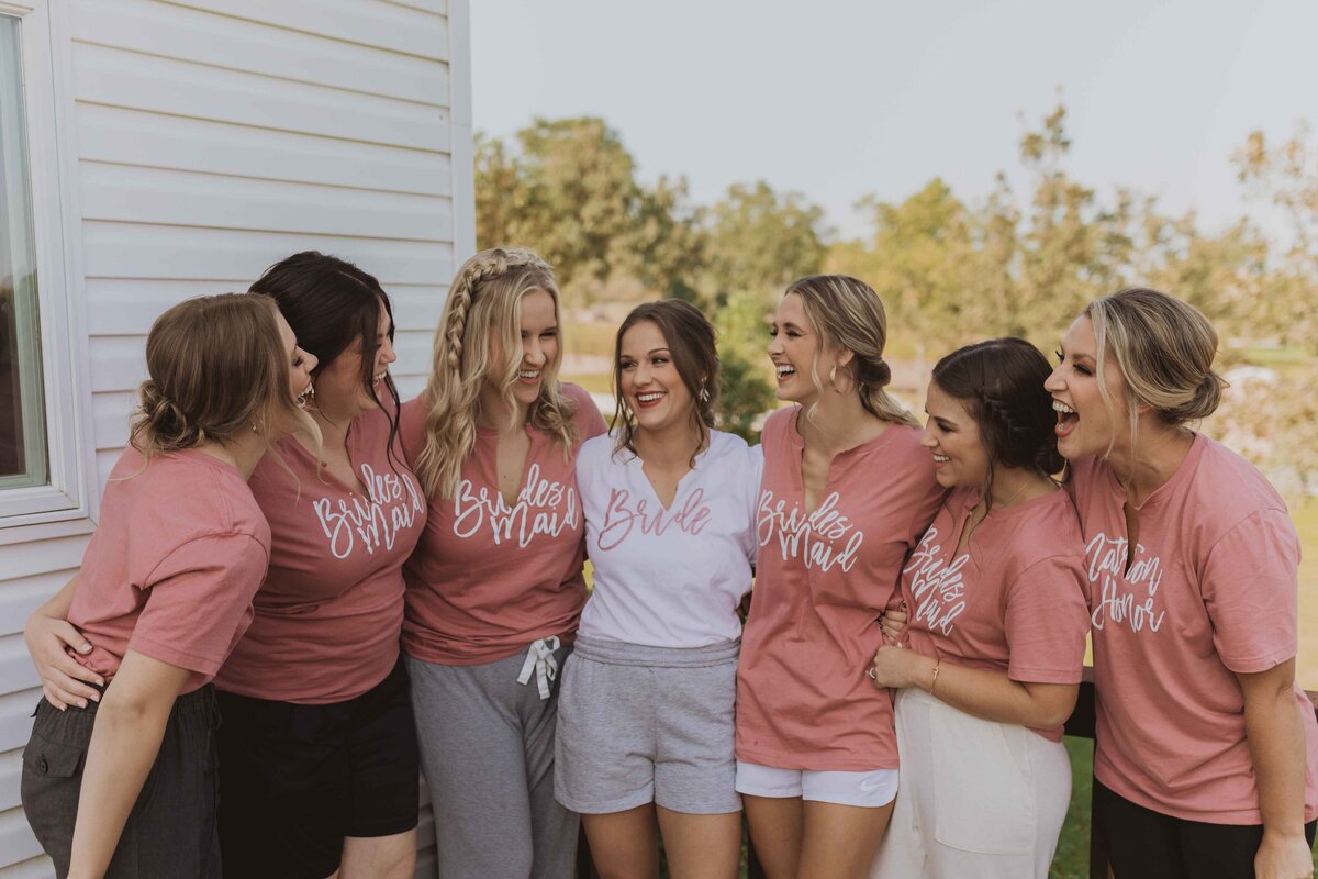 Bride smiling and laughing with her bridesmaids on her wedding day. All wearing matching t-shirts before getting dressed for the wedding.