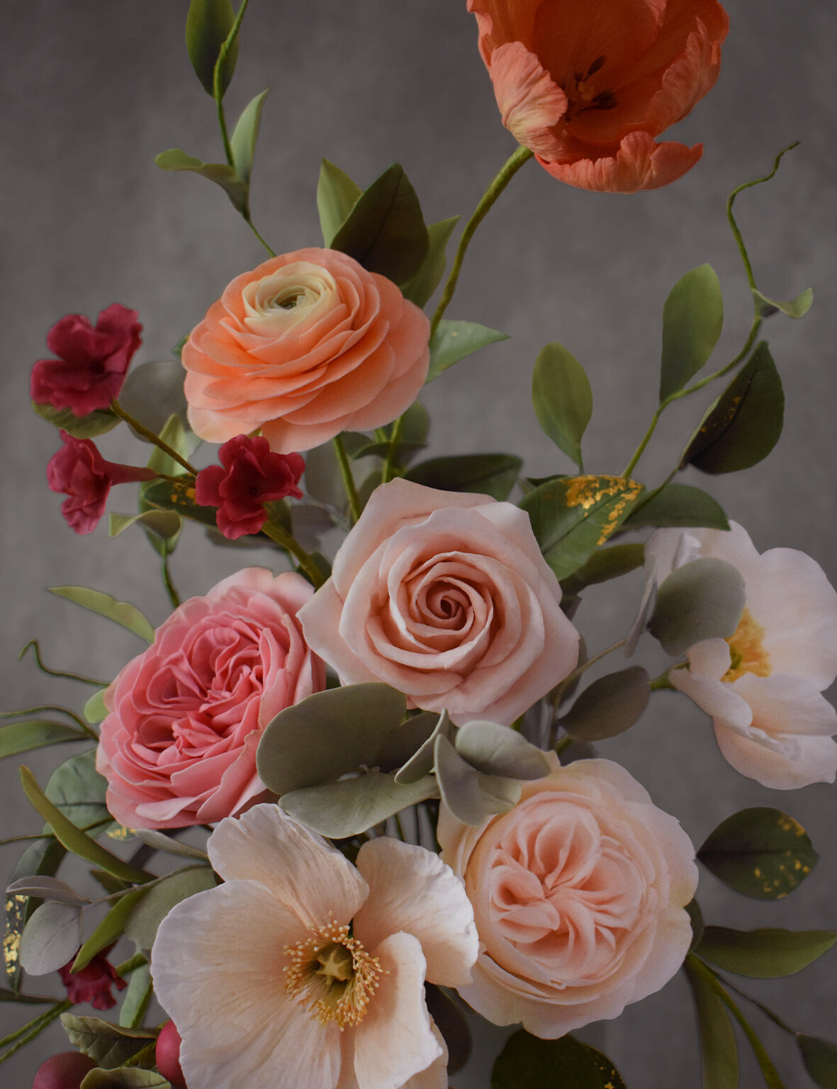 Closeup of sugar flowers including orange parrot tulips, peach ranunculus, pale pink garden roses and an icelandic poppy  with moody background