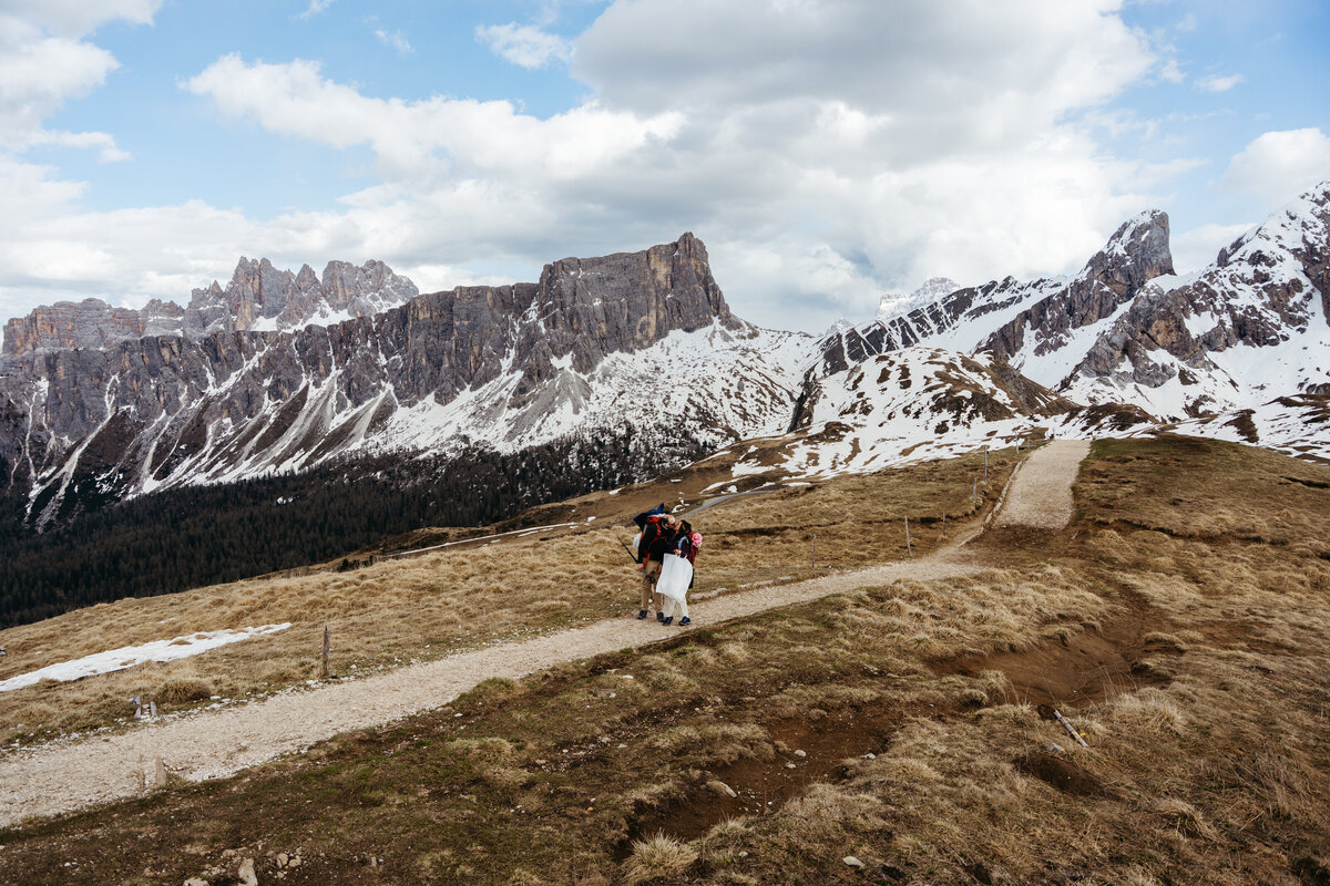 Bride and groom walking mountain trail with snowy peaks behind
