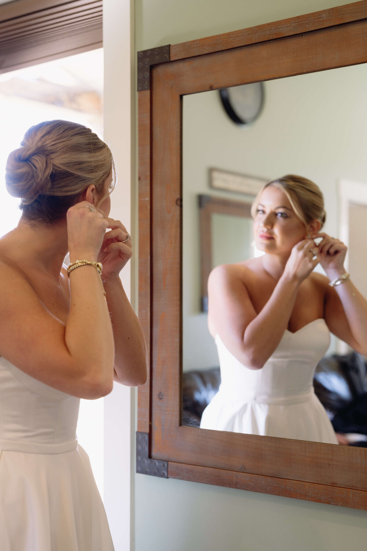bride putting on earrings in a mirror in her at Charlottesville wedding venues bridal suite