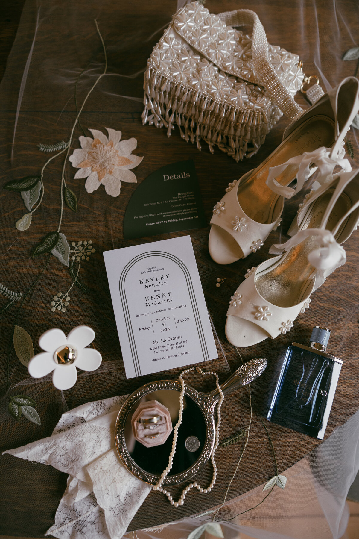 Gorgeous, vintage looking wedding photography overlay of wedding invite, bride’s jewelry, perfume, clutch and shoes with some vintage flowers set on top of a brown natural wood round table captured by Morgan Ashley Lynn Photography in Milwaukee, WI