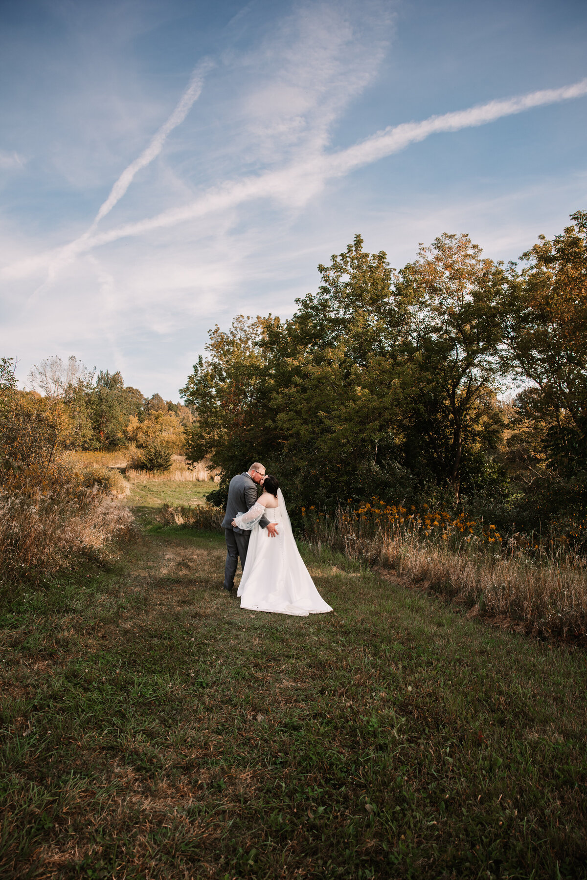 Newlyweds kiss in a grassy trail at sunset